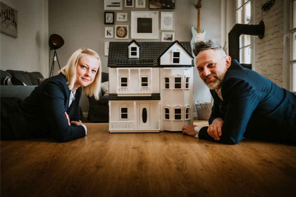 Foto von Juliane und André vor einem Puppenhaus zum Thema Baufinanzierung